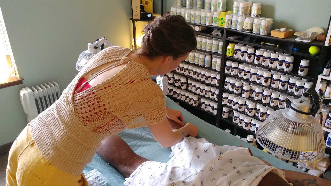 Kat performing acupuncture with Chinese herbs in background