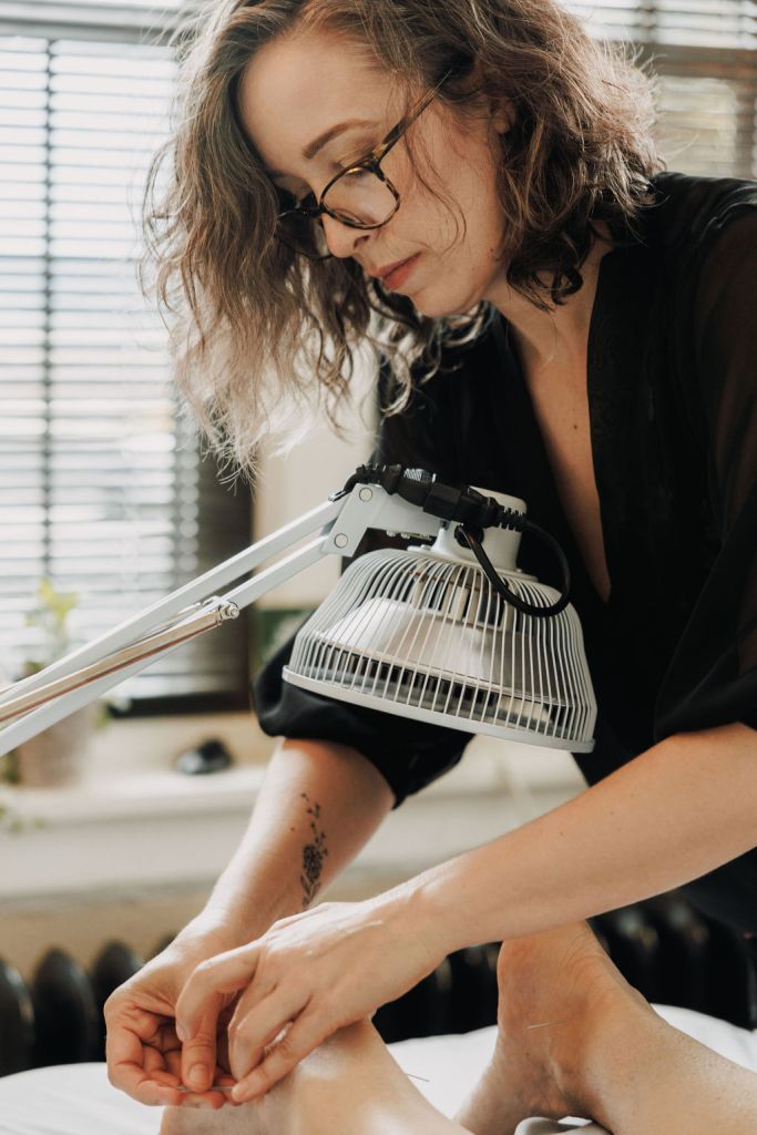 acupuncturist performing acupuncture in a bright room with infrared heat lamp
